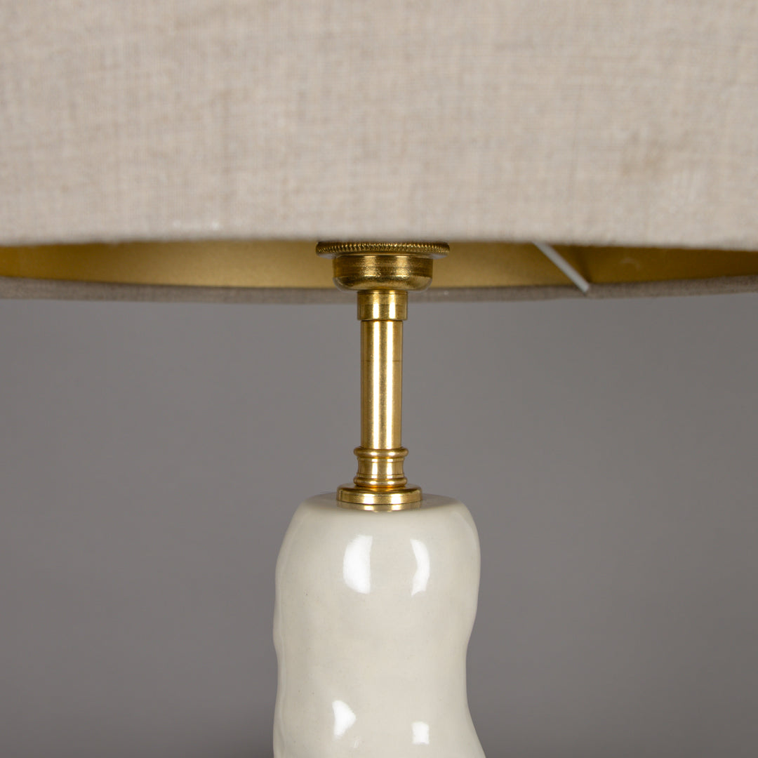 Underside view of the beige linen lampshade with brass fitting – durable and elegant finish for a sculptural table lamp. / Lino gaubto apačia su žalvariniu tvirtinimu – tvirtas ir elegantiškas sprendimas skulptūriniam stalo šviestuvui.