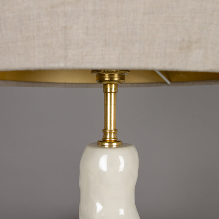 Underside view of the beige linen lampshade with brass fitting – durable and elegant finish for a sculptural table lamp. / Lino gaubto apačia su žalvariniu tvirtinimu – tvirtas ir elegantiškas sprendimas skulptūriniam stalo šviestuvui.