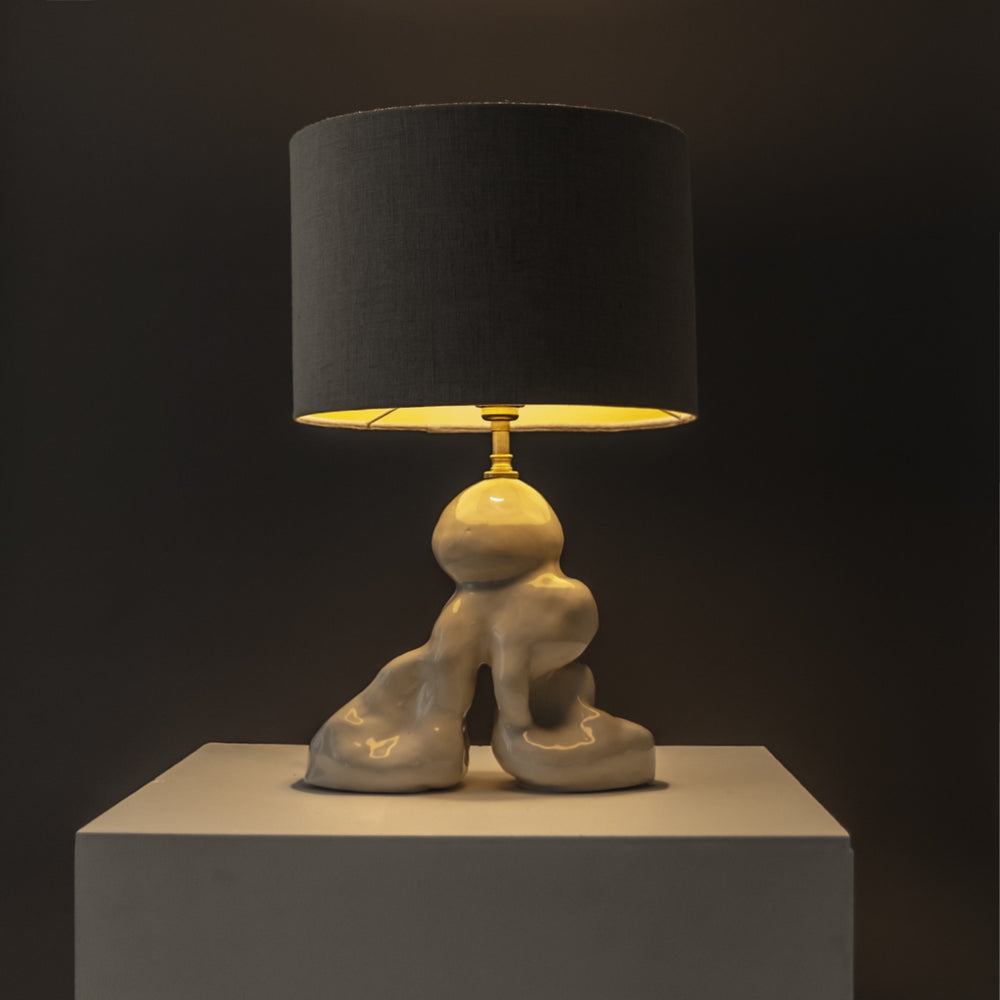 Designer stoneware lamp glowing warmly under a linen shade – ideal for cozy corners and evening ambience. / Dizainerio akmens masės šviestuvas su lininiu gaubtu skleidžia šiltą šviesą – jaukioms namų erdvėms.