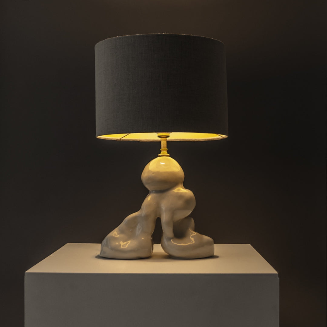 Designer stoneware lamp glowing warmly under a linen shade – ideal for cozy corners and evening ambience. / Dizainerio akmens masės šviestuvas su lininiu gaubtu skleidžia šiltą šviesą – jaukioms namų erdvėms.