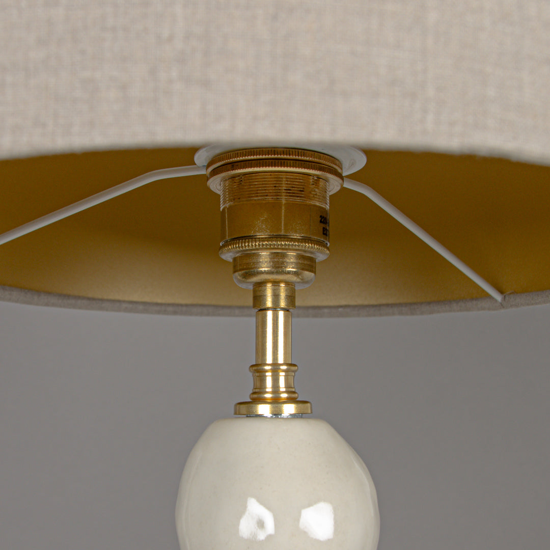 Underside of beige linen lampshade with brass fitting – a high-end finish for stoneware lighting. / Smėlio spalvos lino gaubto apačia su žalvario tvirtinimu – aukštos klasės detalė akmens masės šviestuvui.
