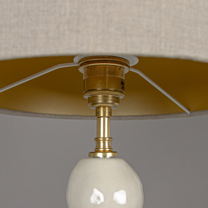 Underside of beige linen lampshade with brass fitting – a high-end finish for stoneware lighting. / Smėlio spalvos lino gaubto apačia su žalvario tvirtinimu – aukštos klasės detalė akmens masės šviestuvui.