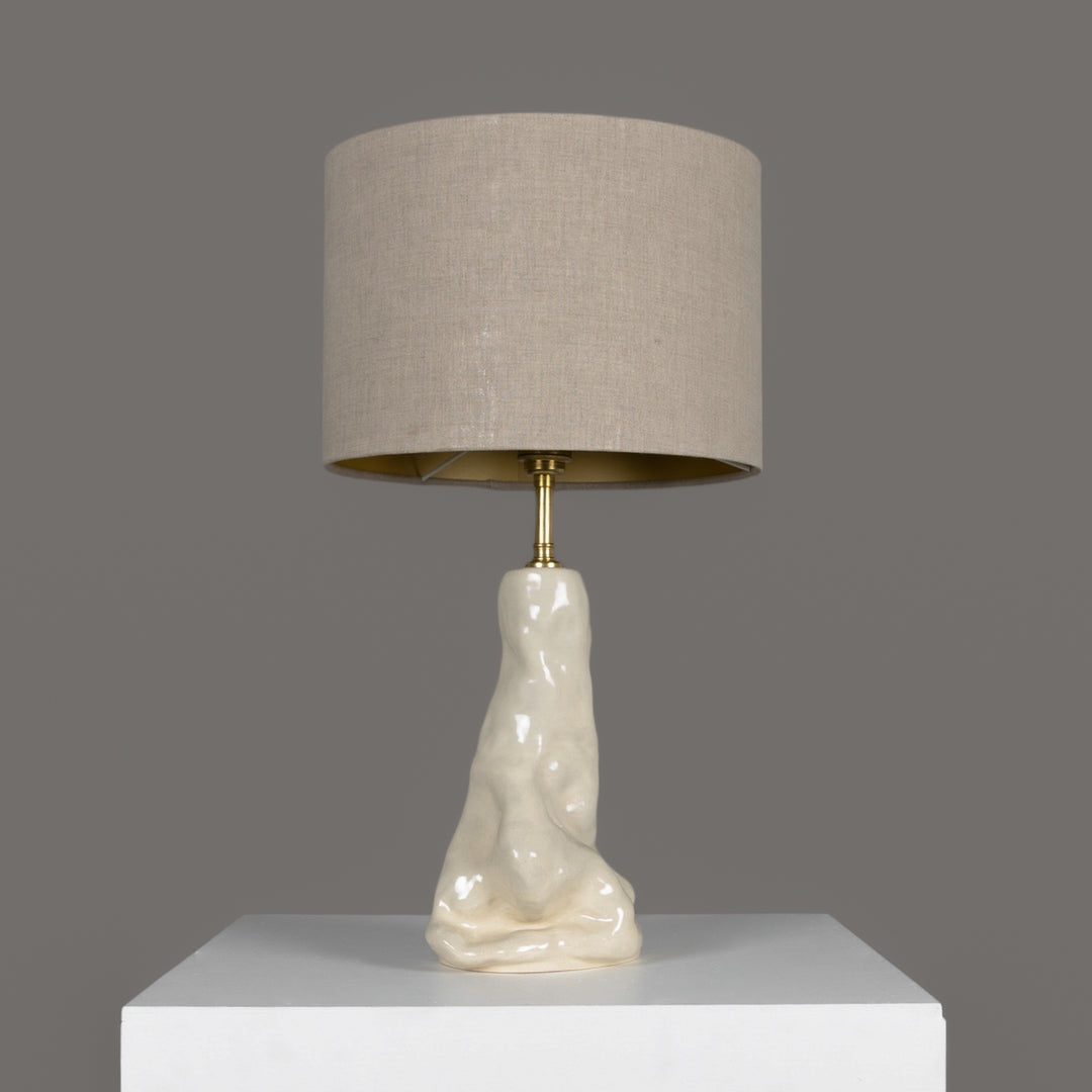 Sculptural stoneware table lamp with beige linen lampshade – elegant ceramic lighting for modern interiors. / Skulptūrinis akmens masės stalinis šviestuvas su šviesiu lino gaubtu – elegantiškas apšvietimas šiuolaikiniam interjerui.