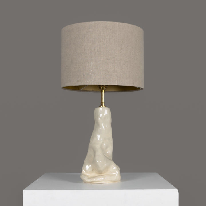 Sculptural stoneware table lamp with beige linen lampshade – elegant ceramic lighting for modern interiors. / Skulptūrinis akmens masės stalinis šviestuvas su šviesiu lino gaubtu – elegantiškas apšvietimas šiuolaikiniam interjerui.