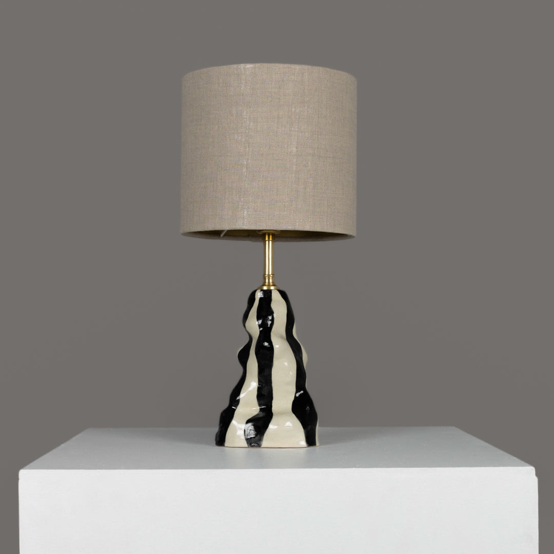 Handmade black and white stoneware table lamp with beige linen lampshade – sculptural lighting for modern and artistic interiors. / Rankų darbo juodai baltas akmens masės stalinis šviestuvas su lino gaubtu – skulptūrinis akcentas šiuolaikiniam interjerui.