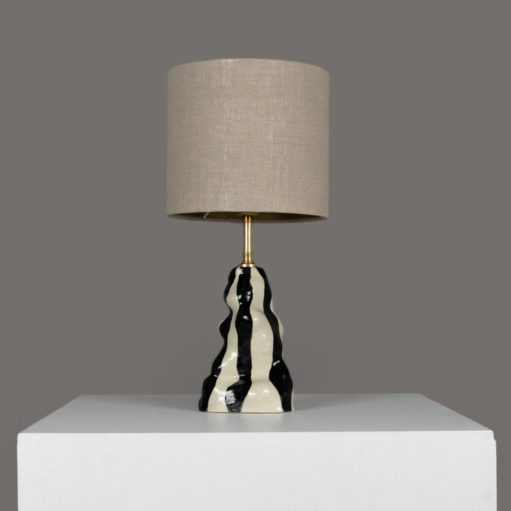 Handmade black and white stoneware table lamp with beige linen lampshade – sculptural lighting for modern and artistic interiors. / Rankų darbo juodai baltas akmens masės stalinis šviestuvas su lino gaubtu – skulptūrinis akcentas šiuolaikiniam interjerui.