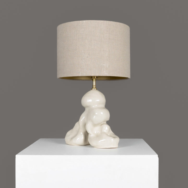 Modern stoneware lamp with linen shade on white stand – timeless lighting for bedrooms or living rooms. / Šiuolaikinis akmens masės šviestuvas su lino gaubtu – laikui nepavaldus apšvietimas miegamajam ar svetainei.