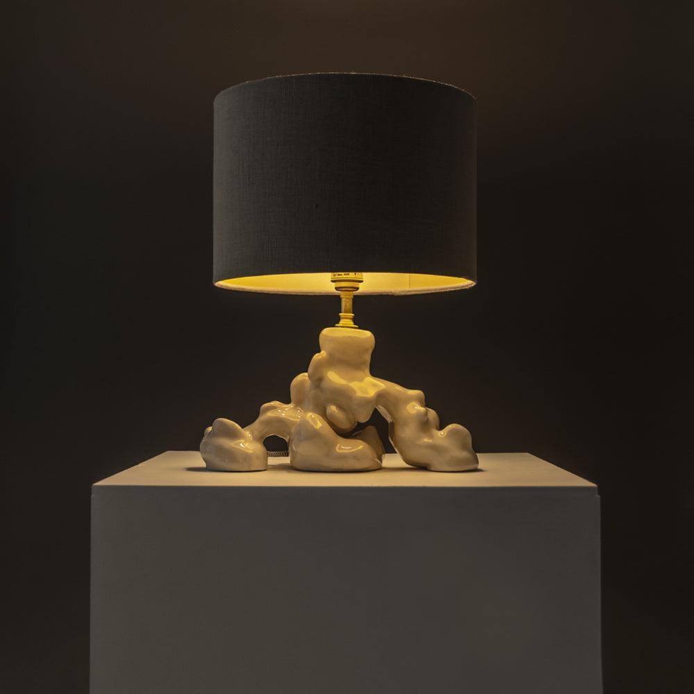 Stoneware lamp with soft golden glow, handmade ceramic base – a refined sculptural light piece for mood-driven settings. / Akmens masės šviestuvas skleidžia šiltą šviesą – rankų darbo skulptūrinis šviesos akcentas.