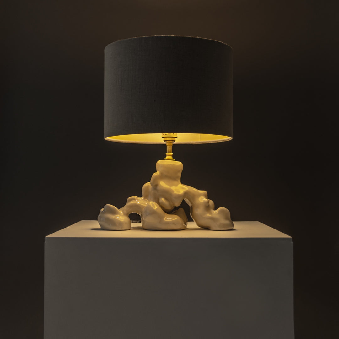 Stoneware lamp with soft golden glow, handmade ceramic base – a refined sculptural light piece for mood-driven settings. / Akmens masės šviestuvas skleidžia šiltą šviesą – rankų darbo skulptūrinis šviesos akcentas.