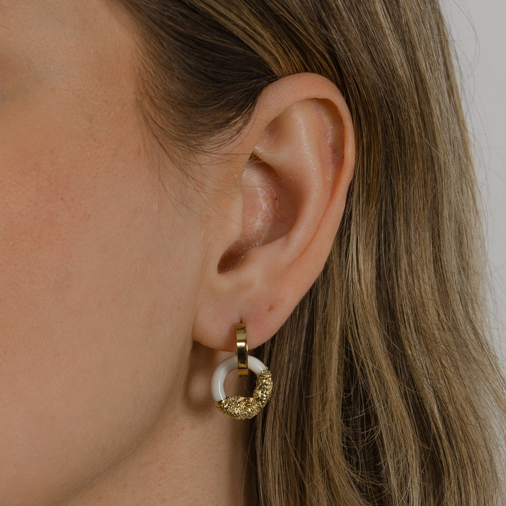 Freakyfoxx nuotrauka, kurioje matyti ausis su mažu auksiniu ir baltu žiediniu auskaru neryškiame fone.