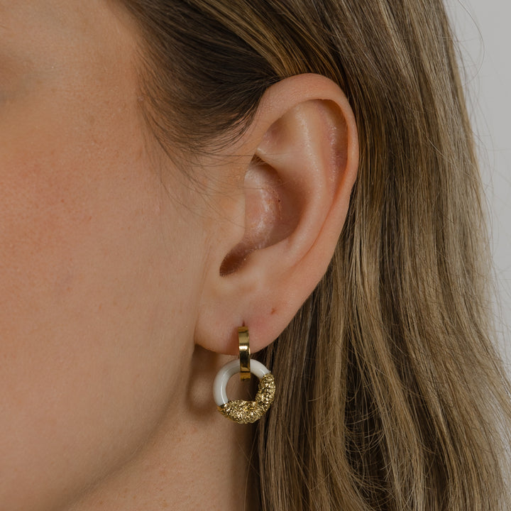 Freakyfoxx nuotrauka, kurioje matyti ausis su mažu auksiniu ir baltu žiediniu auskaru neryškiame fone.