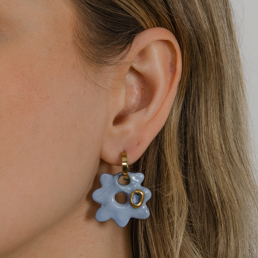 Ausies su šviesiai mėlynu gėlėtu auskaru su auksiniu centru stambus planas. 