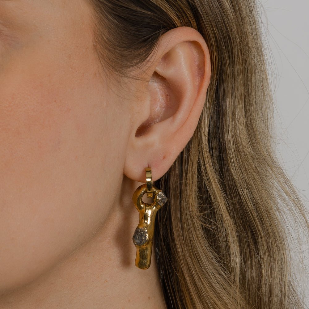 Close-up of a person wearing a unique gold porcelain charm with hoop earring by freakyfoxx