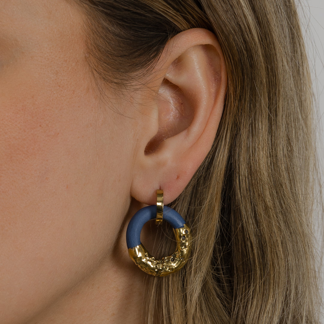 Close-up of an ear wearing a blue and gold hoop earring.