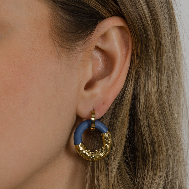 Close-up of an ear wearing a blue and gold hoop earring.