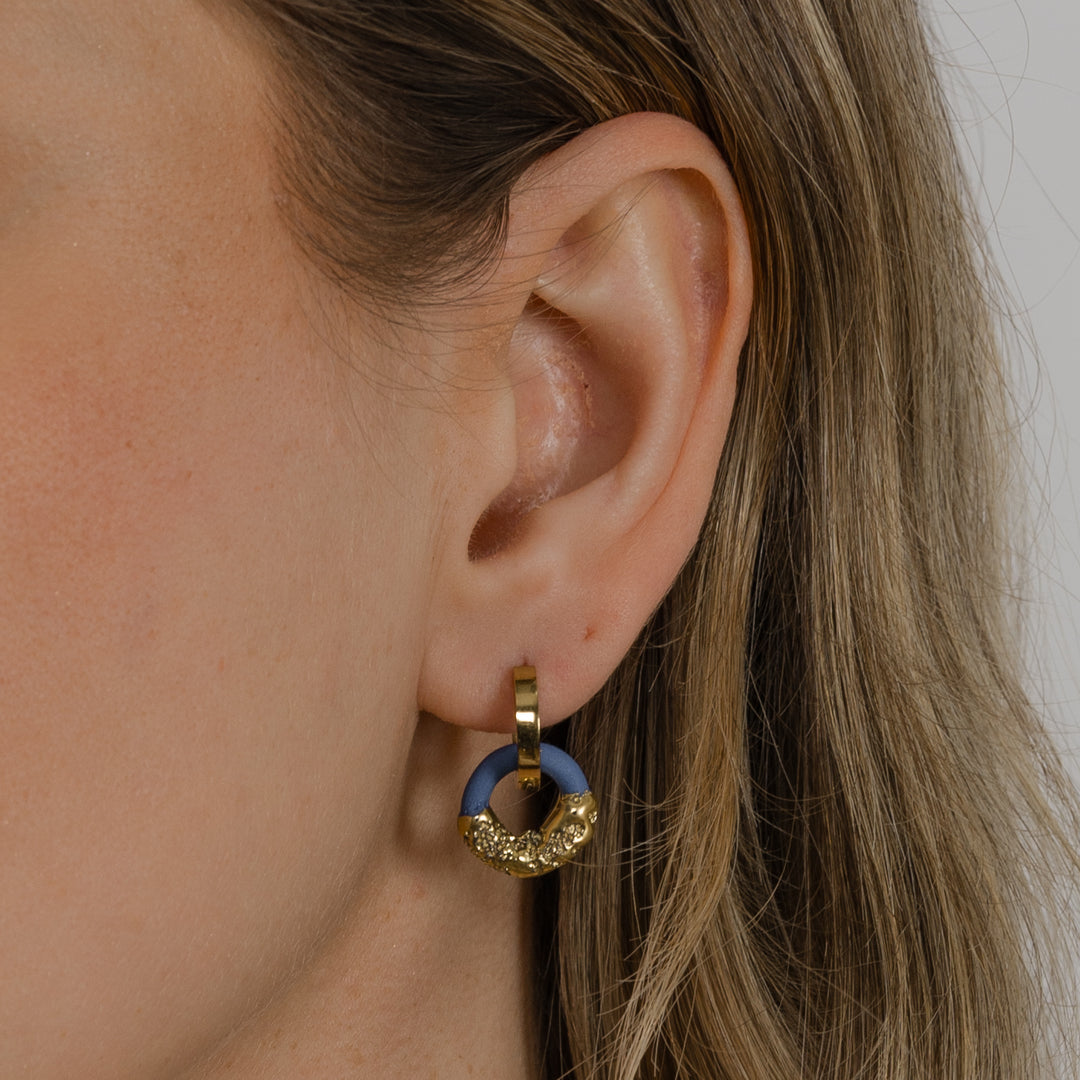 Close-up of an ear wearing a gold and blue earring.