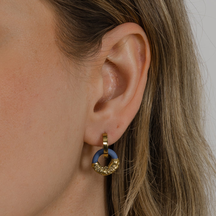 Close-up of an ear wearing a gold and blue earring.