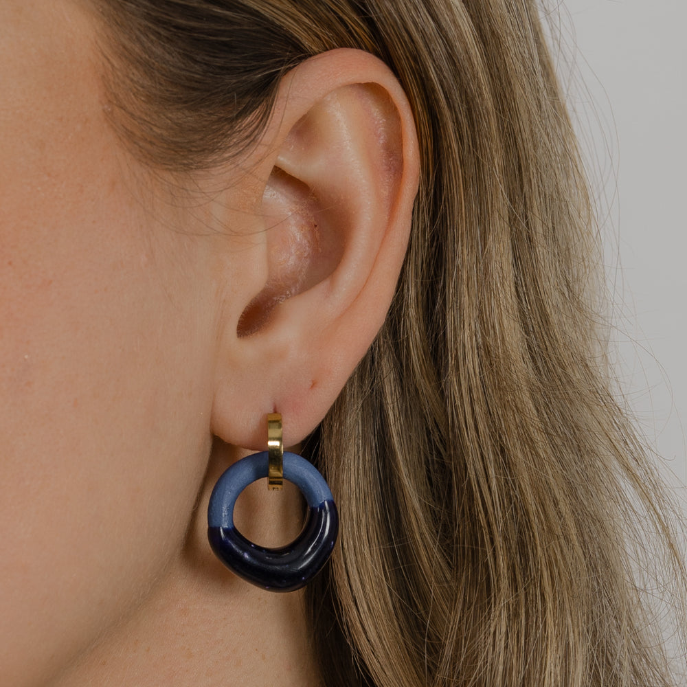 Close-up of an ear wearing a blue hoop earring with a gold accent.