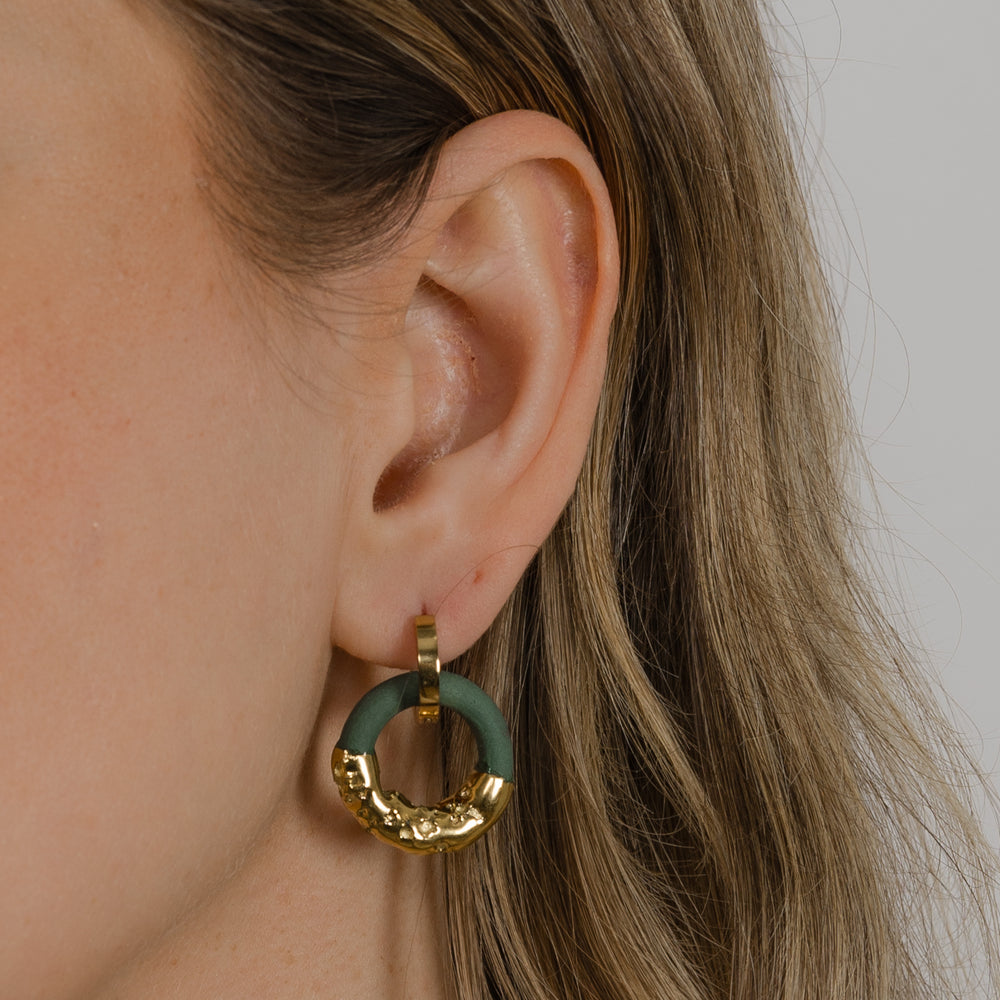 Close-up of an ear wearing a gold and green hoop earring against a neutral background