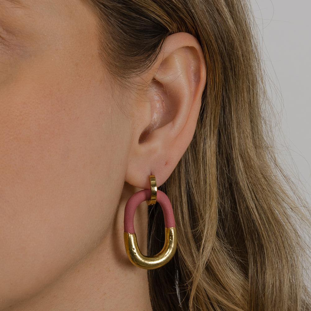 Ausis su auksiniu ir rožiniu žiediniu auskaru neutraliame fone, stambus planas