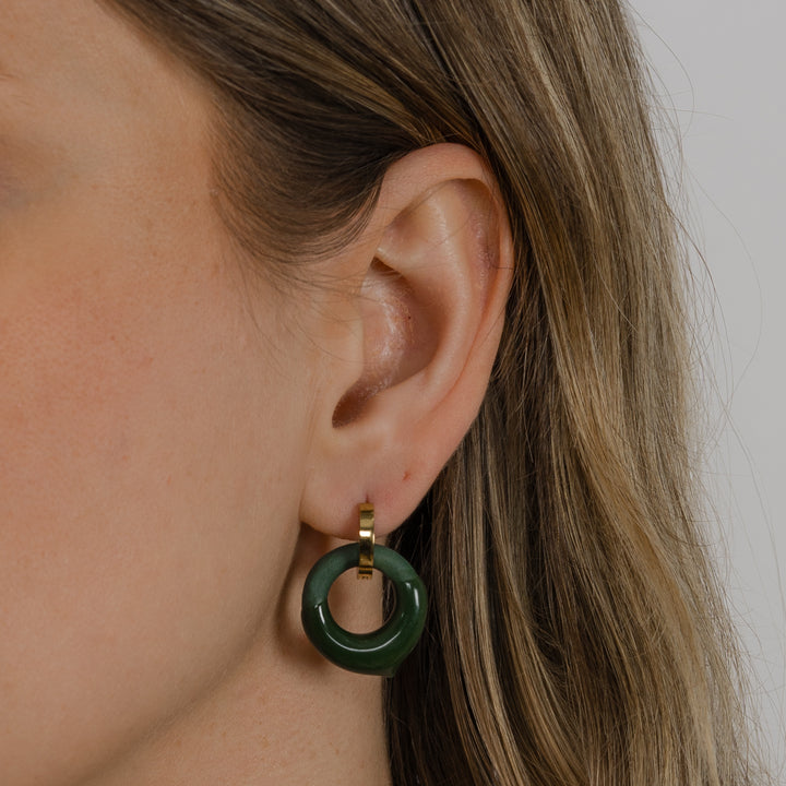Close-up of an ear wearing a handmade green hoop earring by freakyfoxx with a neutral background
