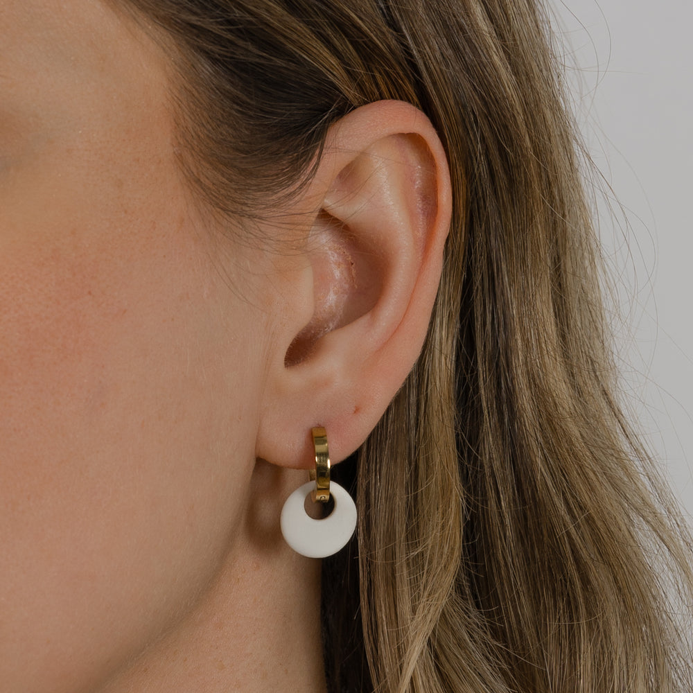 Close-up of an ear wearing a gold hoop earring with a white matte circular pendant.