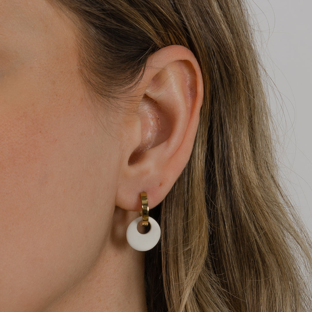 Close-up of an ear wearing a gold hoop earring with a white matte circular pendant.