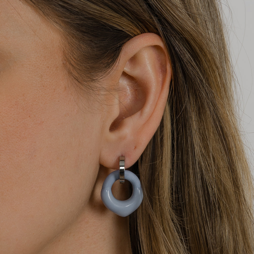 Close-up of an ear wearing a light blue porcelain charm with hoop earring