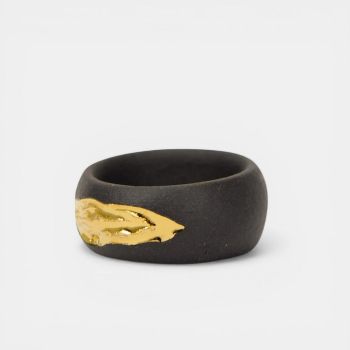 Black porcelain ring with gold leaf design on a light gray background