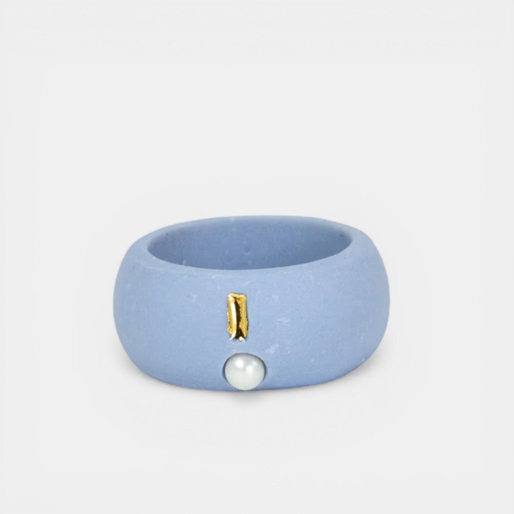 Blue ring with a gold accent and pearl on a light gray background