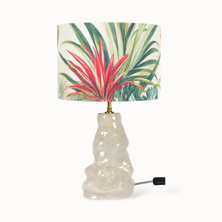 Handmade ceramic table lamp with a sculptural glossy base and a botanical linen blend lampshade featuring tropical plants.
Rankų darbo keraminis stalo šviestuvas su skulptūriniu blizgiu pagrindu ir botaniniu lininio mišinio gaubtu, dekoruotu tropinių augalų motyvais