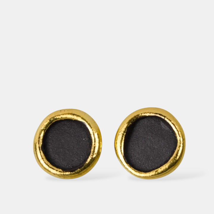 Pair of gold-framed black matte round porcelain earrings on a light gray background by FreakyFoxx