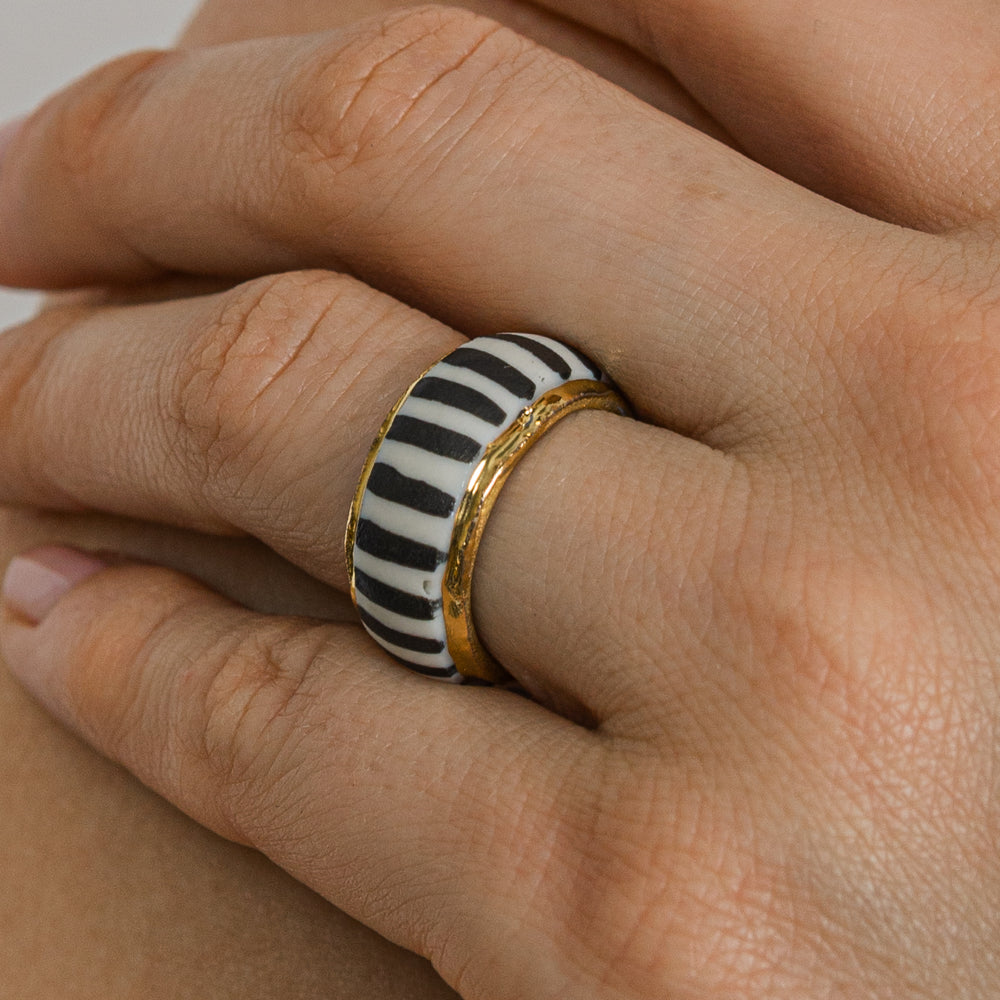 Hand wearing a ring with black and white striped design on a light background
