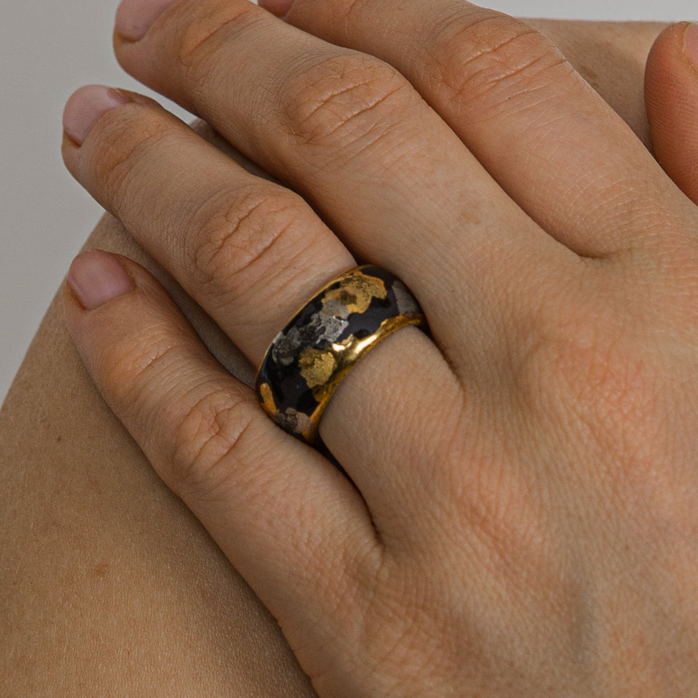 Hand wearing a ring with a gold and black design on a neutral background