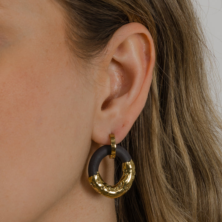 Close-up of an ear wearing a gold and black hoop earring.