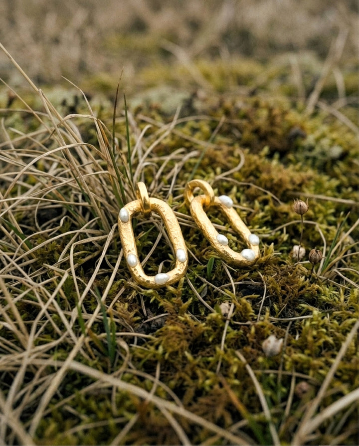 Gold earrings with pearls on a grassy background