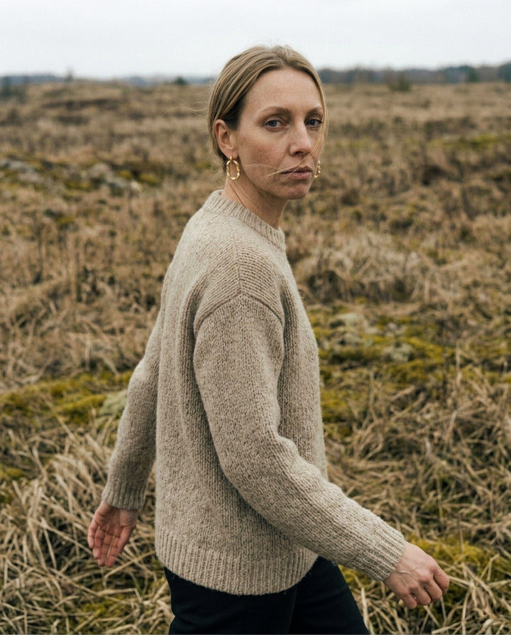 Woman wearing a beige sweater standing in a field with dry grass and a cloudy sky. She wears porcelain earrings by freakyfoxx.