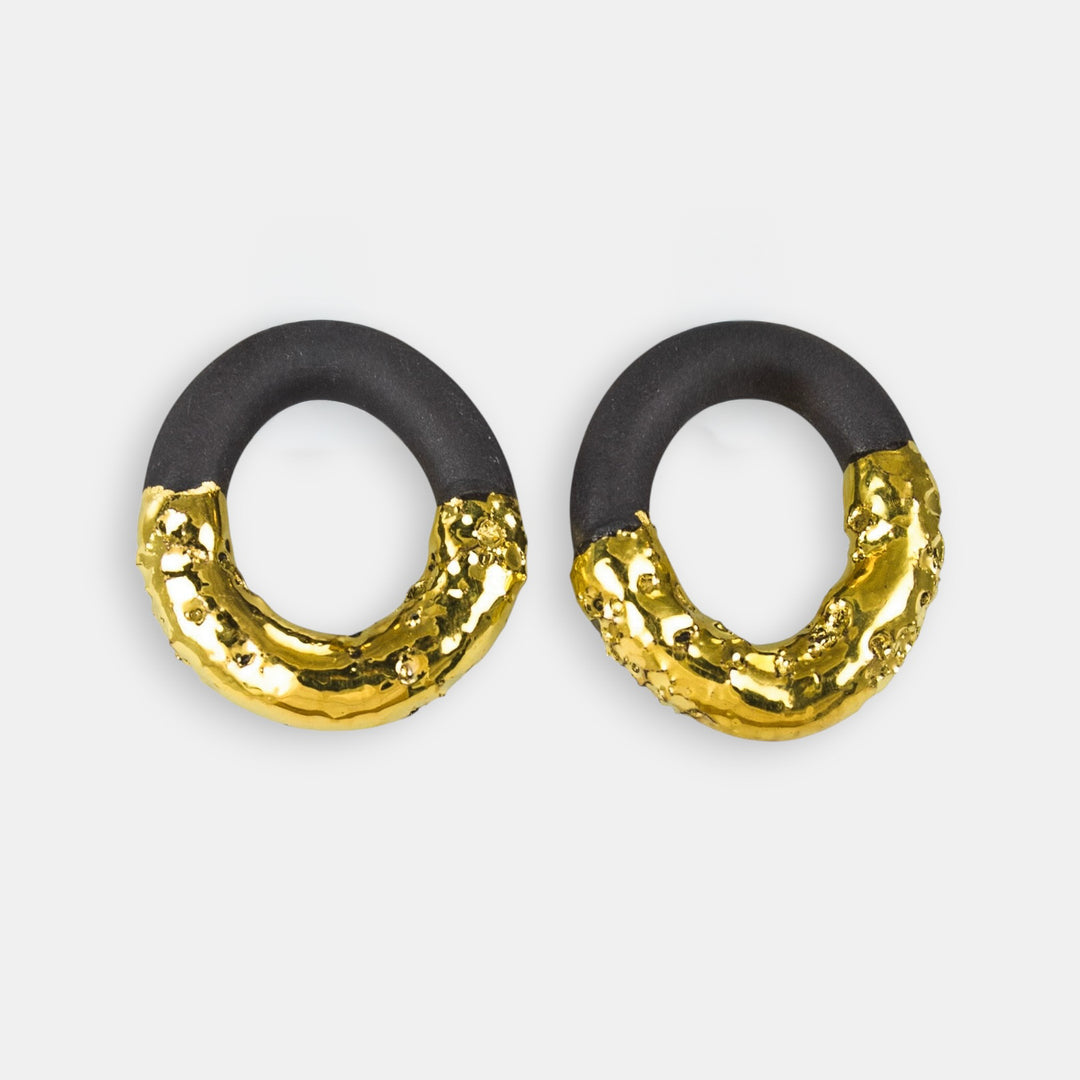 Pair of earrings with black and gold circular design on a light gray background