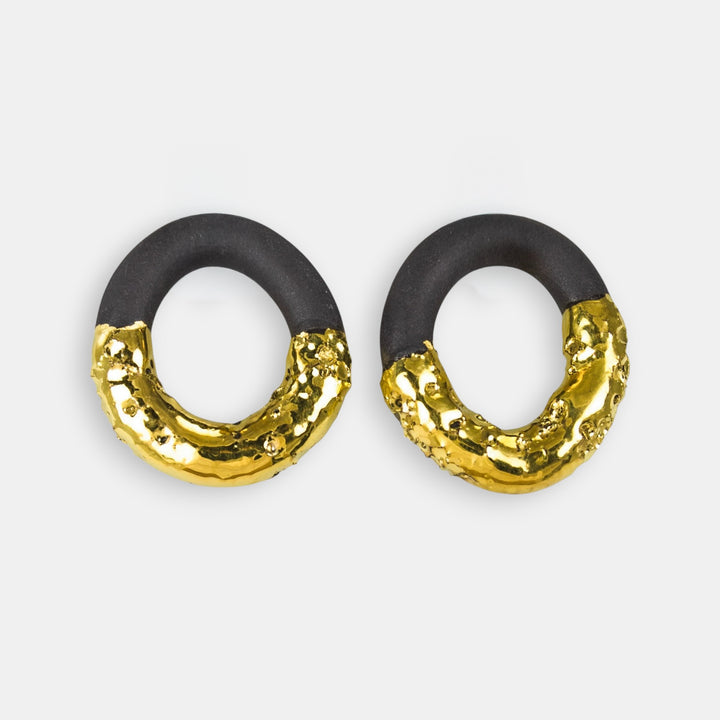 Pair of earrings with black and gold circular design on a light gray background