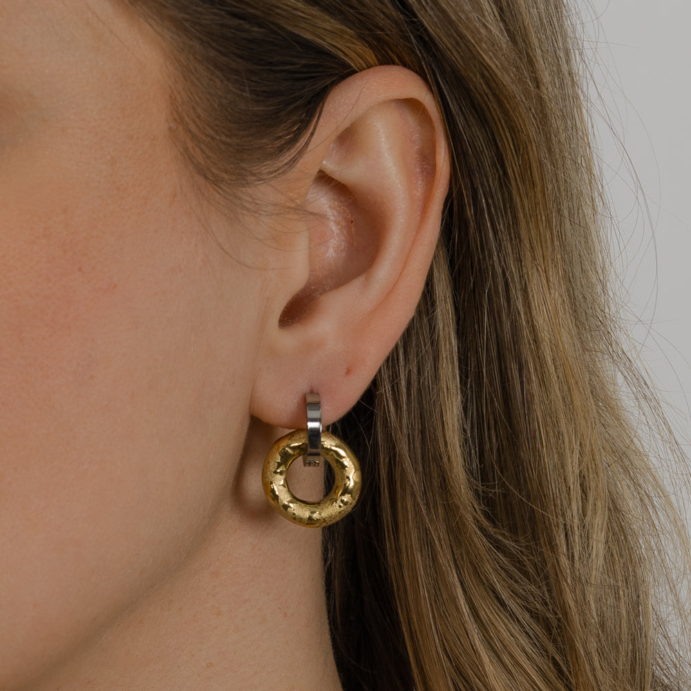 Close-up of a person wearing a gold hoop earring with a neutral background