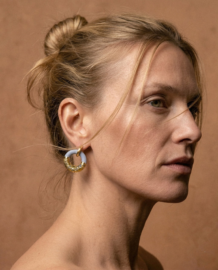 Close-up of a woman wearing a unique ceramic earring against a brown background
