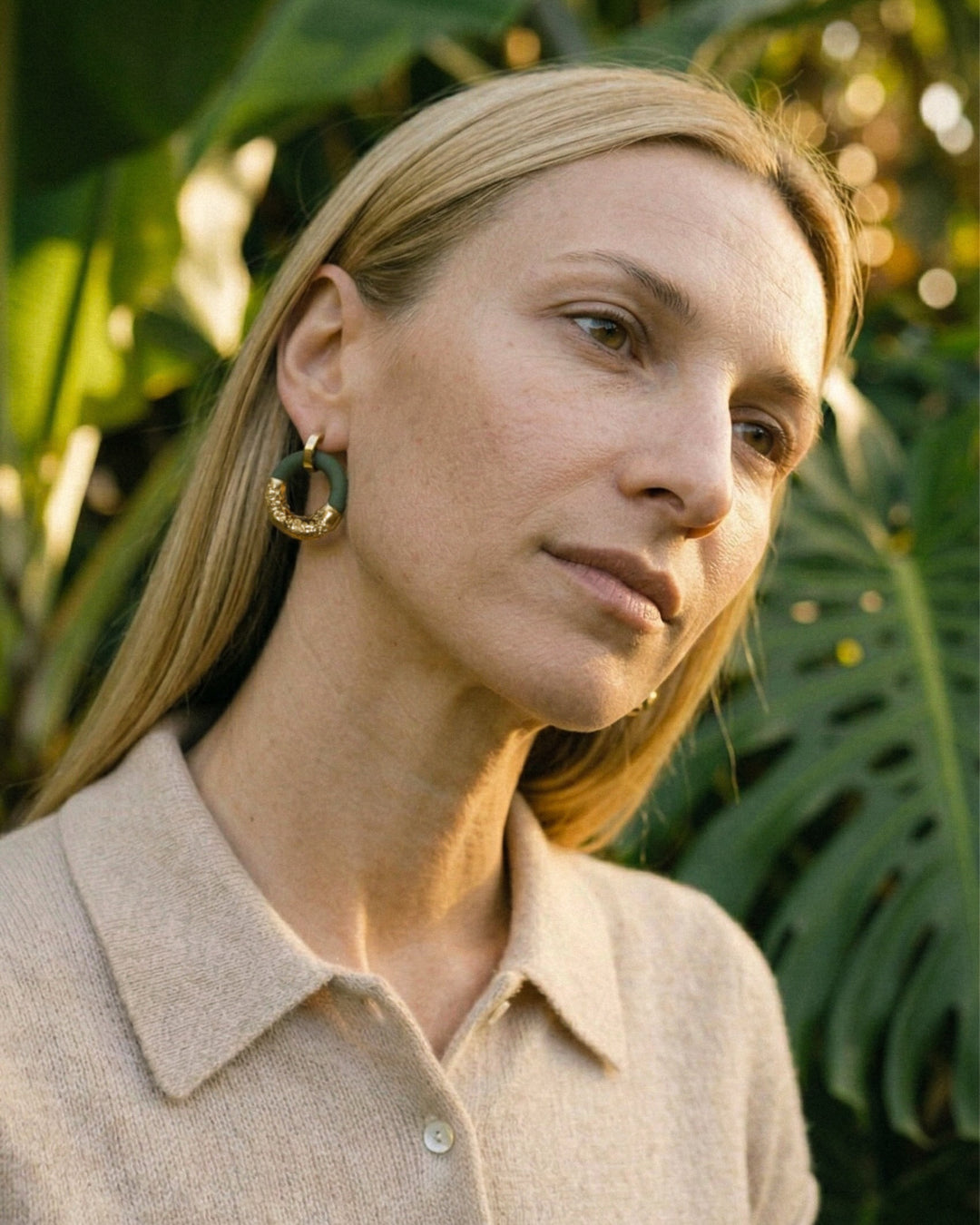 Moteris nešioja žalius porcelianinius žiedinius auskarus žaliame lapiniame fone