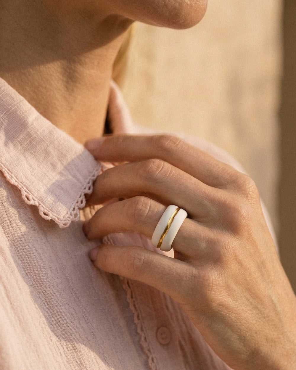 Close-up of a hand wearing a white porcelain ring with gold band on a blurred background