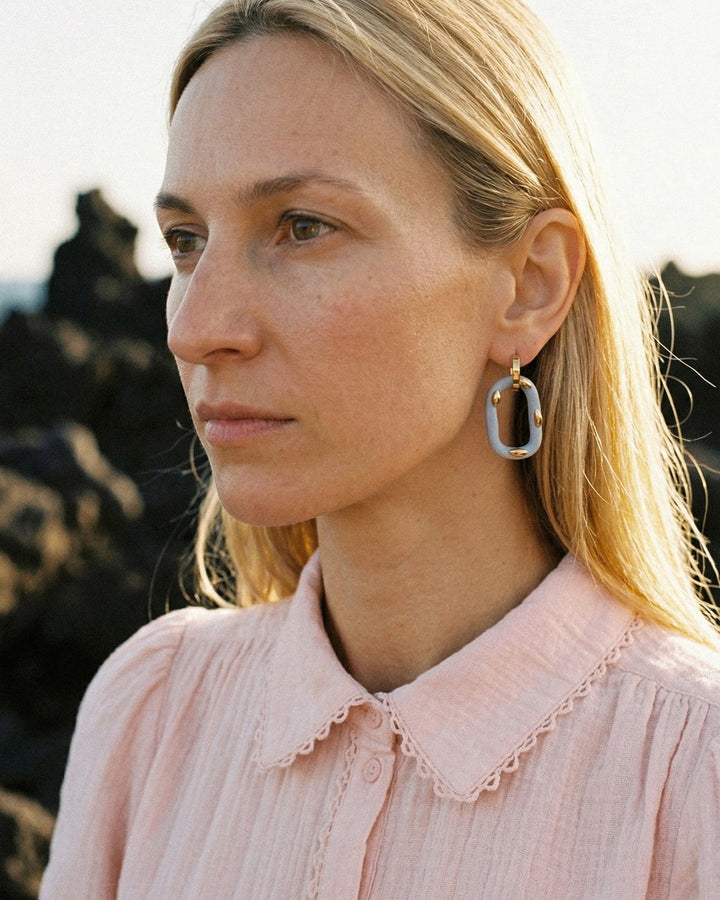 moteris nešioja auksinius žiedinius auskarus su porcelianiniu pakabuku, kuriuos Tenerifėje pagamino freakyfoxx