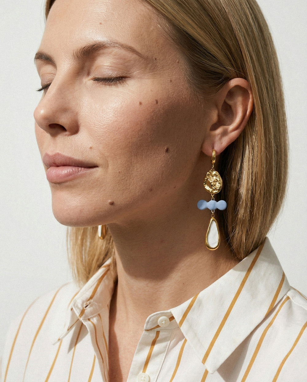 Šviesiaplaukės moters unikalaus, vienetinio auskaro su mėlynai baltu porcelianu stambaus plano šviesiame fone vaizdas