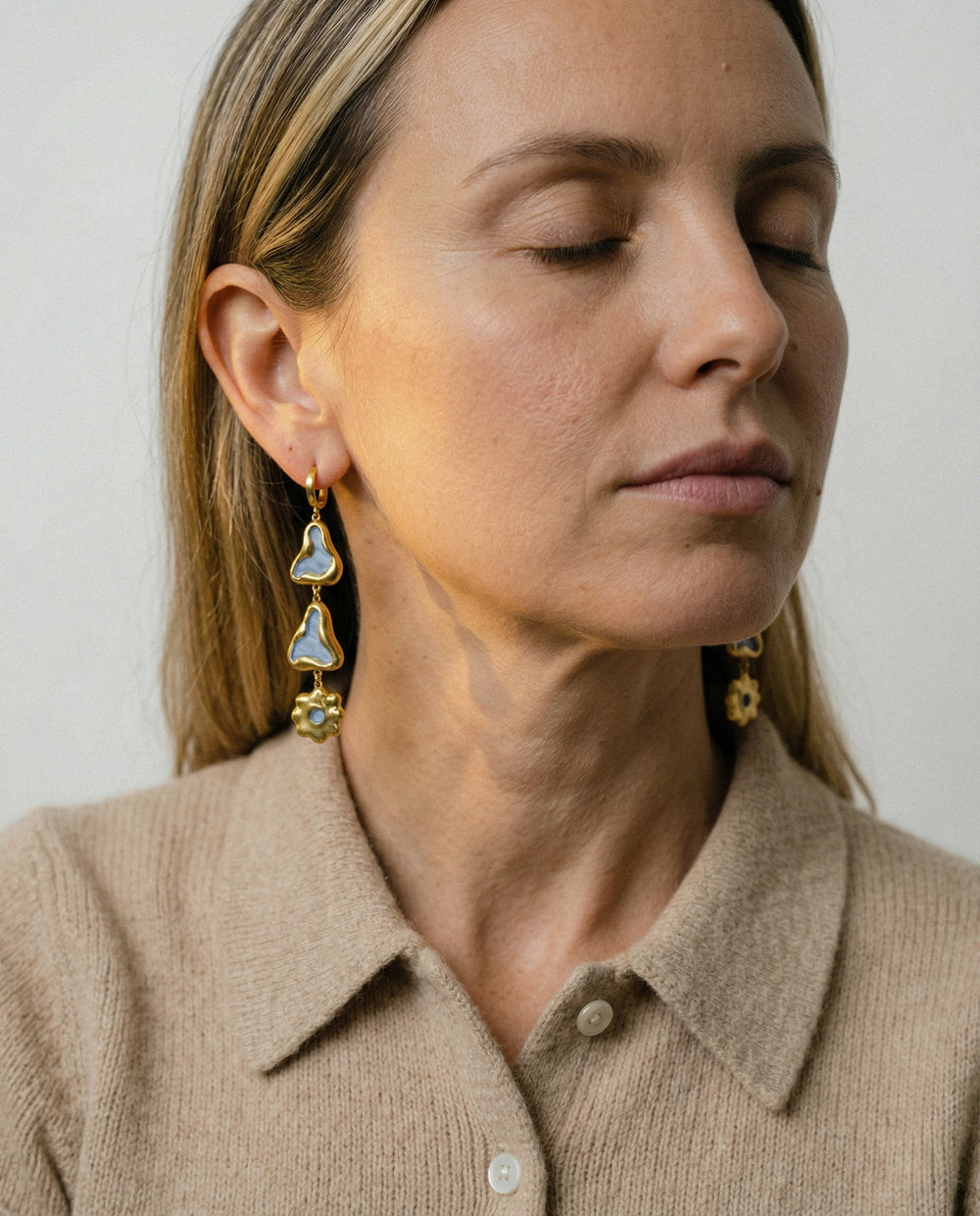 Moteris su unikaliais širdies formos porcelianiniais auskarais, padengtais auksu, neutraliame fone