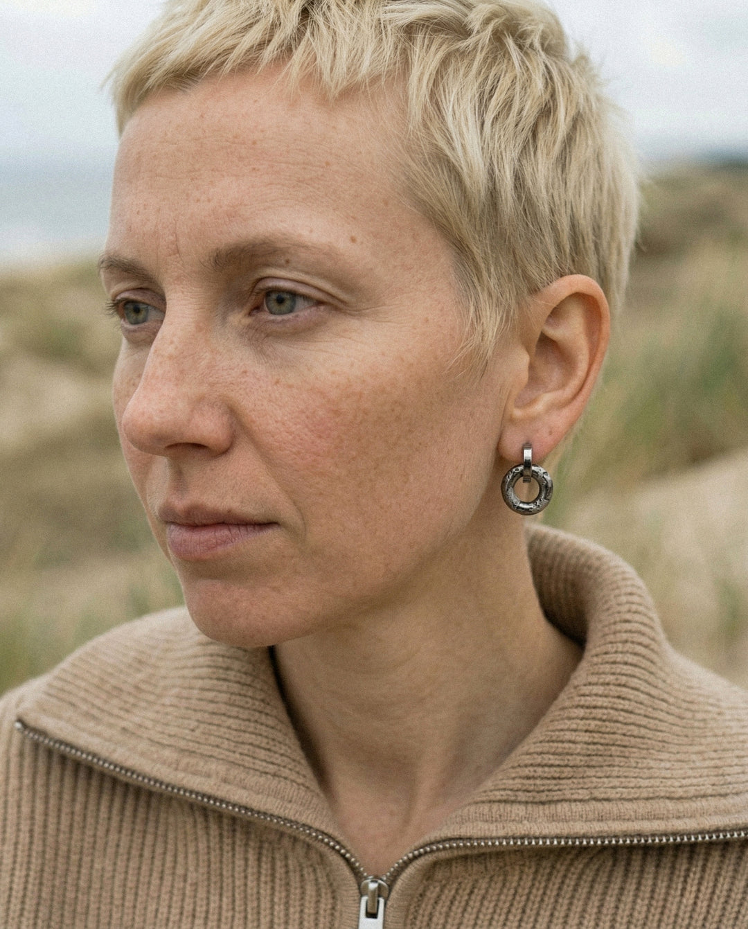 Moteris trumpais šviesiais plaukais, seginti rankų darbo porcelianinį auskarą