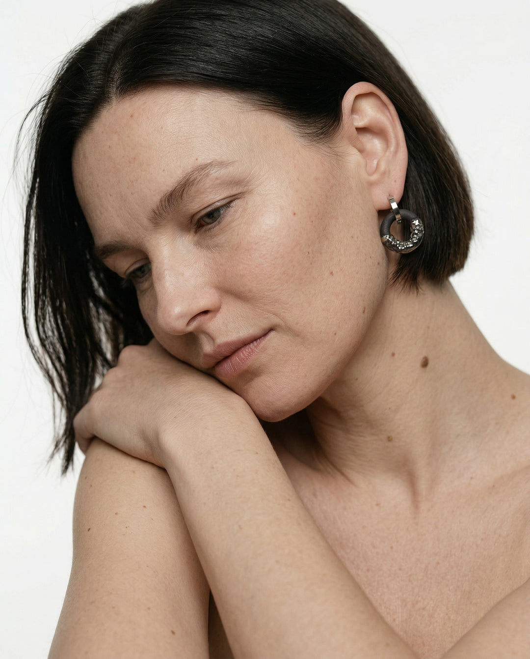 Moteris trumpais tamsiais plaukais, nešiojanti sidabrinį žiedinį auskarą su porcelianiniu pakabuku (freakyfoxx) baltame fone