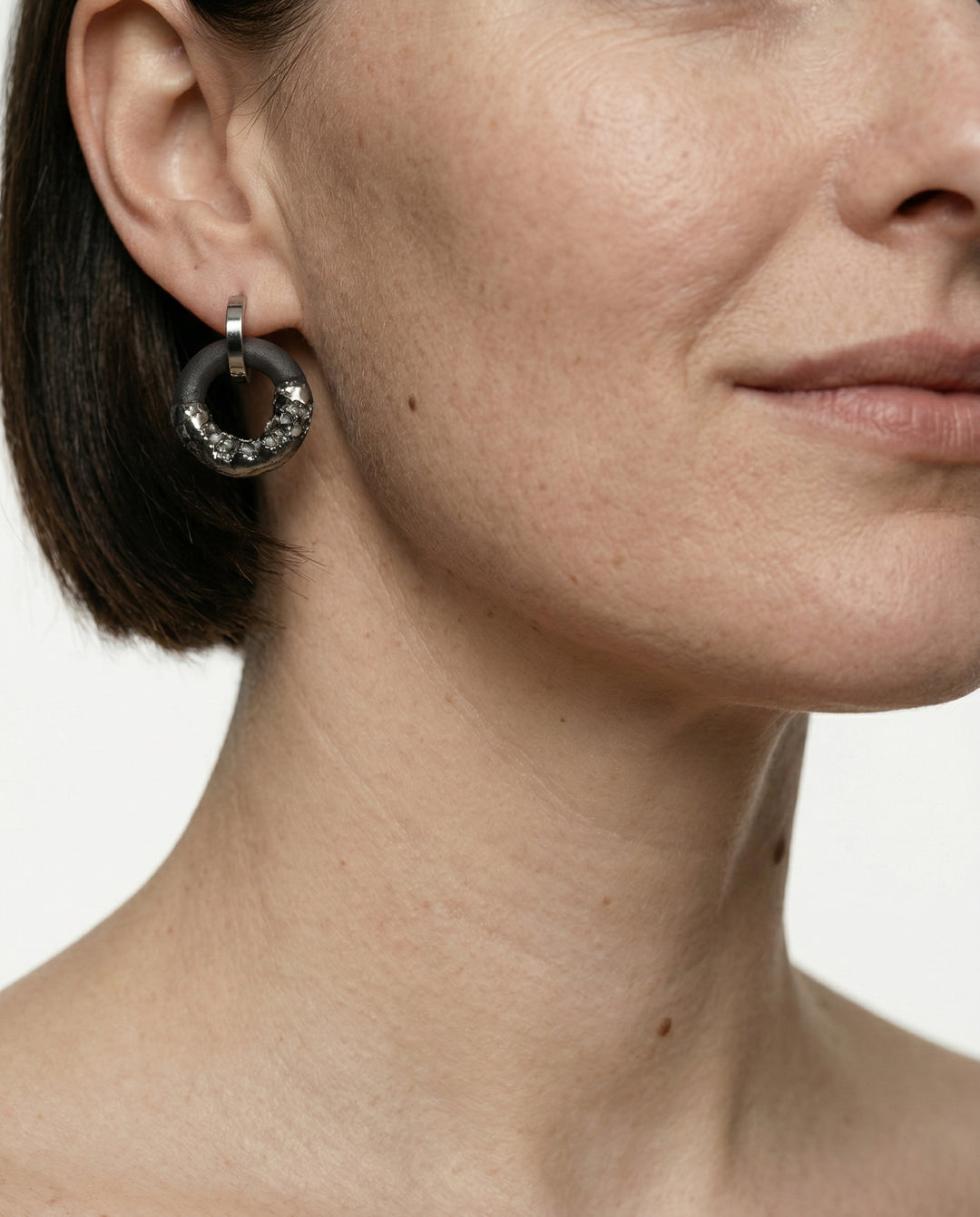 Moteris su sidabriniu žiediniu auskaru ir juodu porcelianiniu pakabuku baltame fone stambaus plano nuotrauka (kūrėjas freakyfoxx)