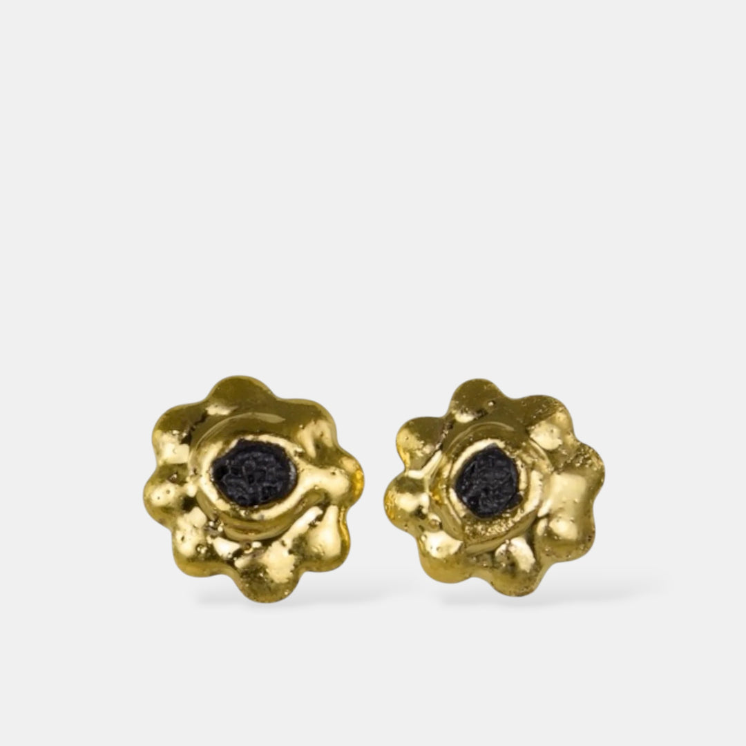 Pora auksinių gėlės formos porcelianinių auskarų su juodais centrais baltame fone